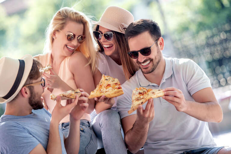 Putt-Putt Fun Center® young adults eating pizza outside wearing sunglasses and smiling